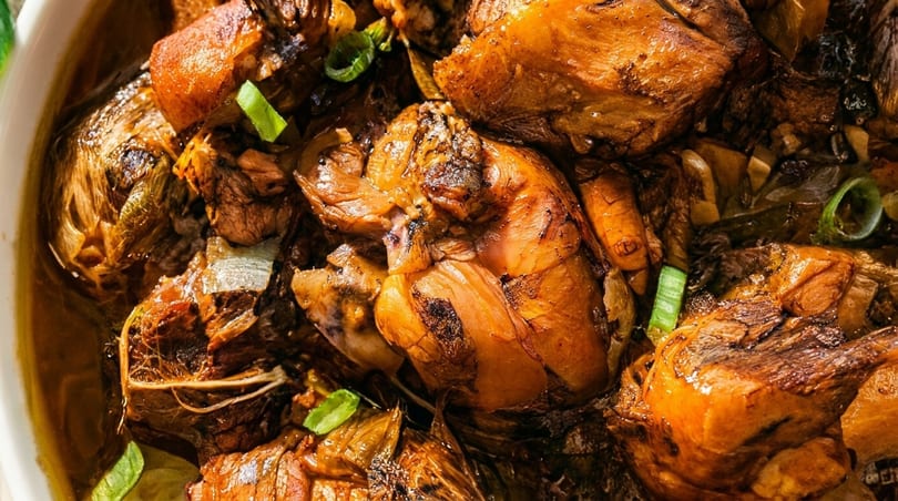 Close-up of savory braised chicken pieces with onions and green garnish in a rich sauce.